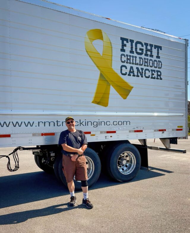 Man standing in front of RM Trucking trailer that says fight childhood cancer on it.